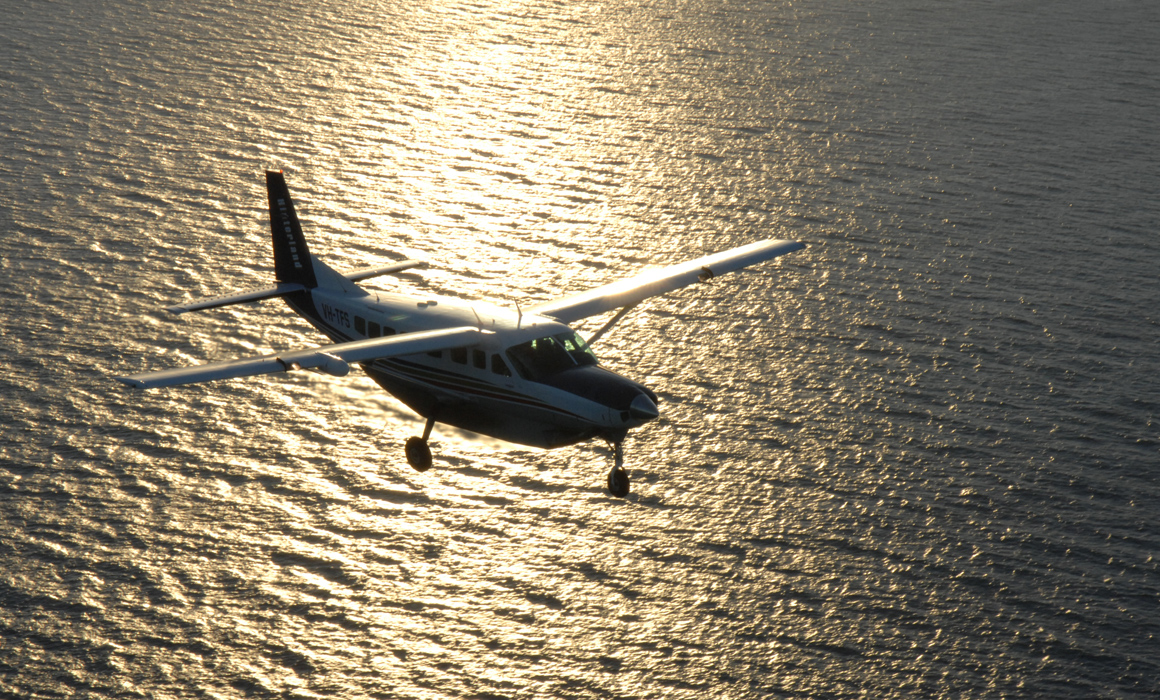 Cessna 208B Grand Caravan flying over water near Cairns at sunset. Gold tones across the surface of the water.