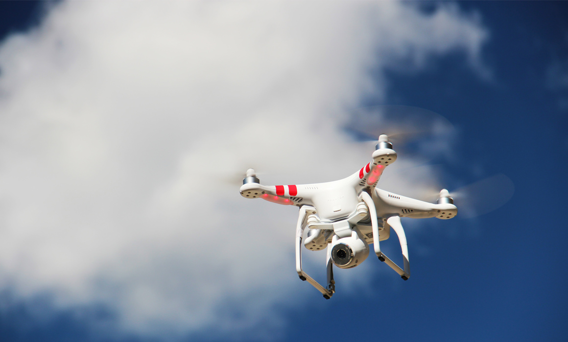 Drone flying against white clouds in a blue sky.