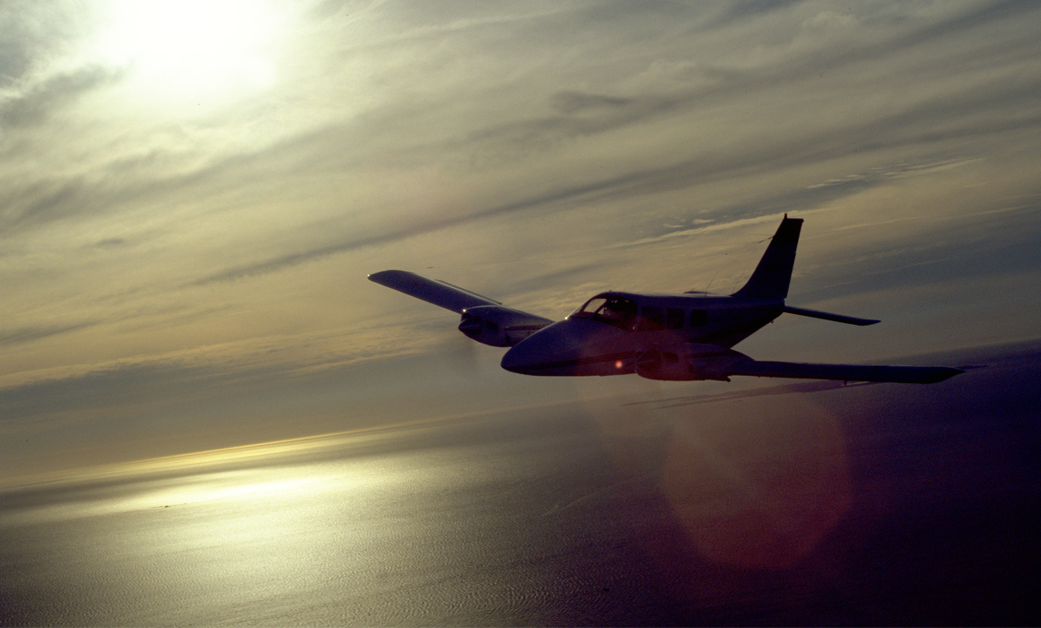 Piper PA-34-200 Seneca flying over water near Perth at sunset.
