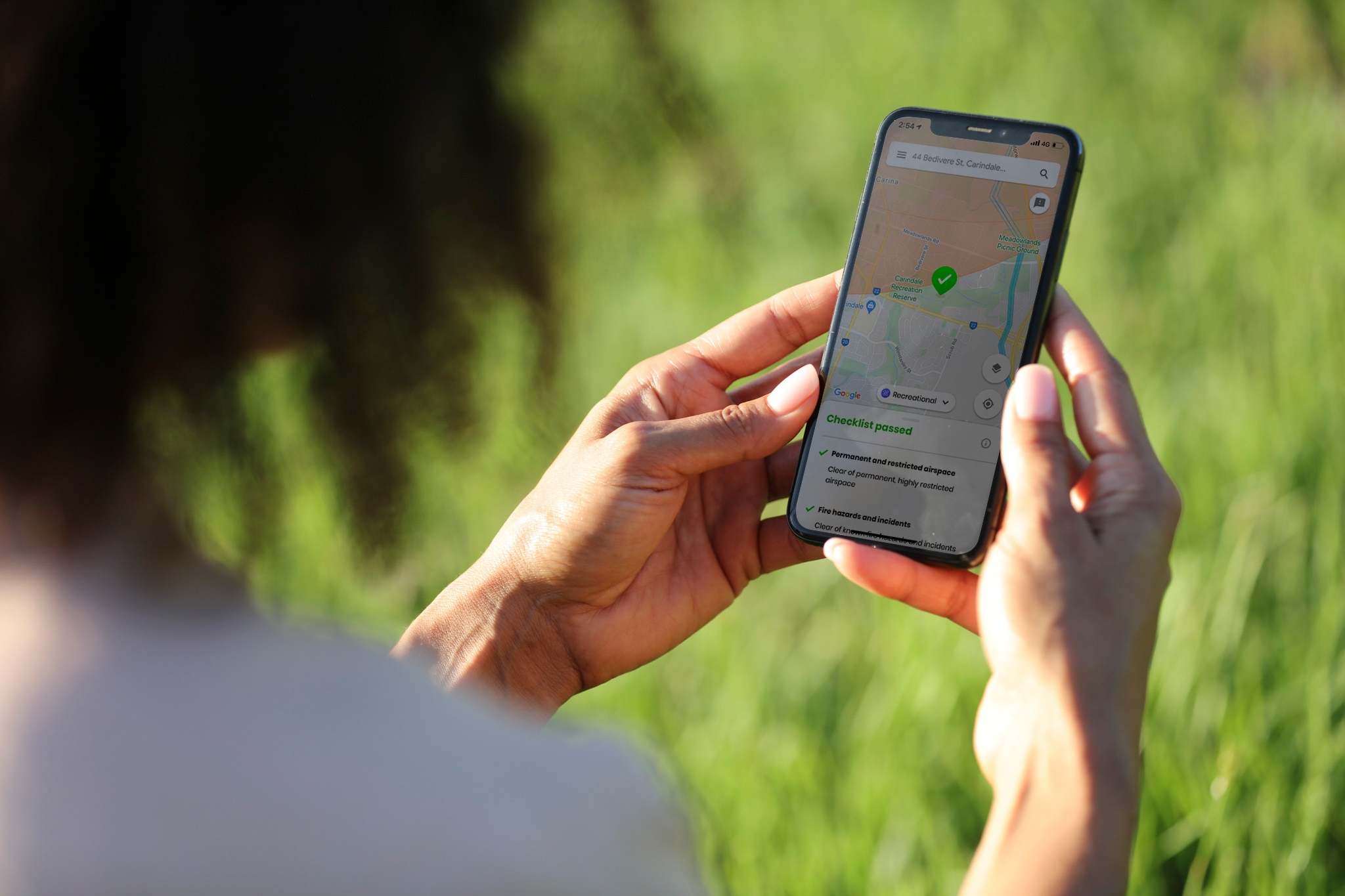 A woman holding a phone displaying a drone safety app's map screen