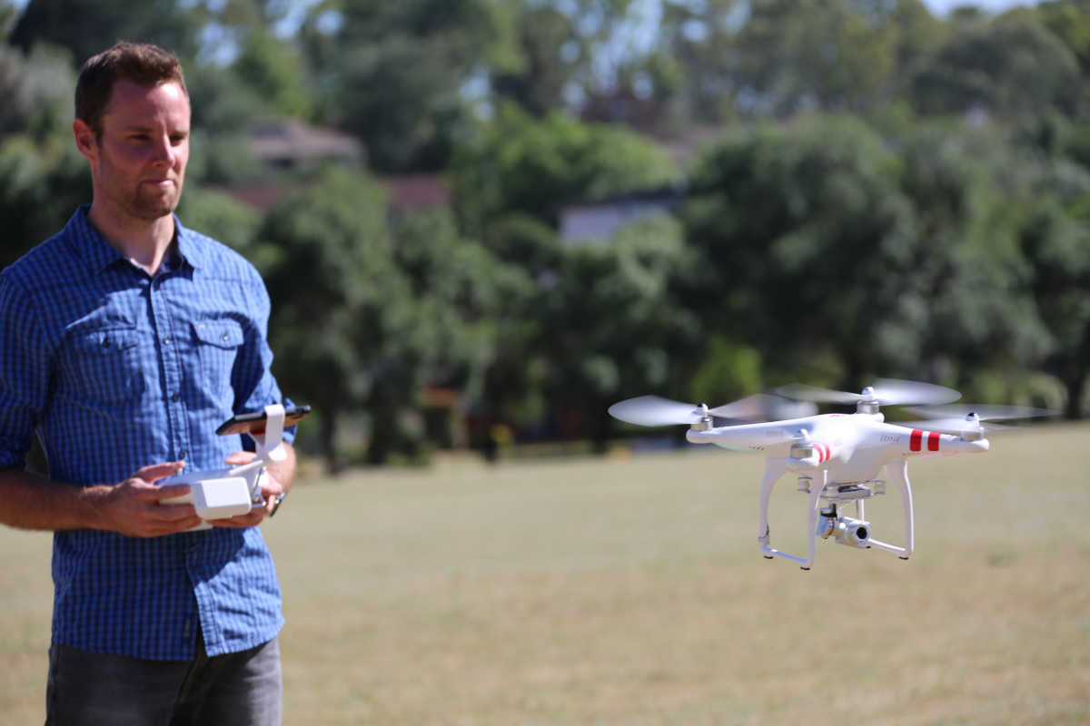 A man flying a white drone in a field with trees in the background