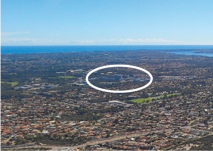 An aerial photo of a suburb, with the Fiona Stanley Hospital sitting in the distance, with a white oval drawn around it