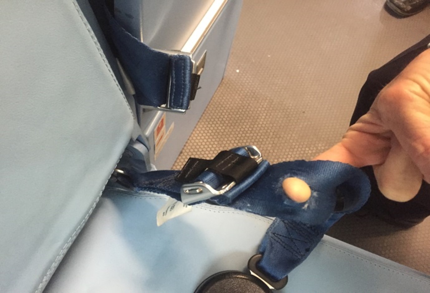 A damaged crew harness on an aircraft, with a hole that an inspector is putting their finger through