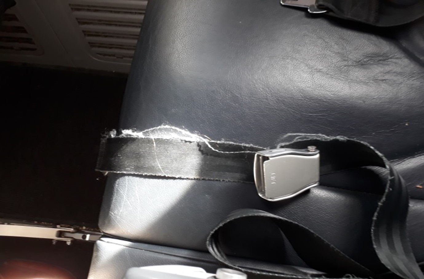 A passenger seatbelt in an aircraft, frayed along the edges of the belt