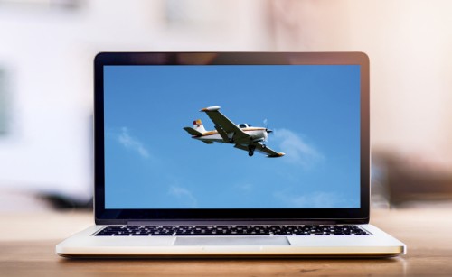 A picture of a flying airplane on the screen of a laptop on a table