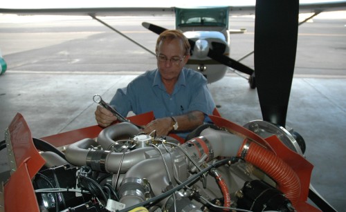 A man maintaining an engine with an small aeroplane parked behind him