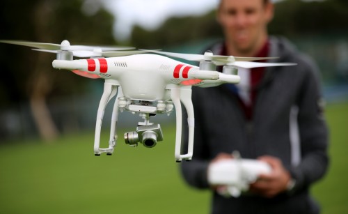 A white drone being flown by a man standing behind it