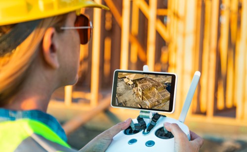 Female Unmanned Aircraft System (UAV) quadcopter drone pilot with controller inspecting new house framing