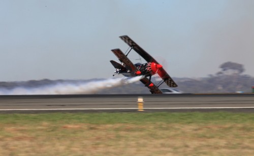 Avalon airshow biplane flying over runway with contrail