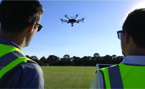 Two men in high-visibility jackets looking at a drone they are flying