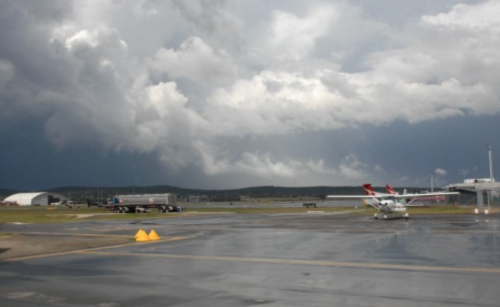 A wet airport taxiway under a cloudy sky