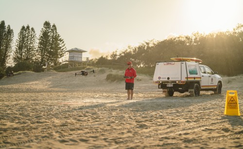 A surf life saver standing on the beach piloting a drone