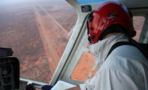 A pilot flying a plane coming in for a landing at a dirt runway