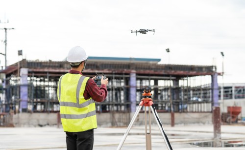 A drone with a man standing behind it holding the remote control for it
