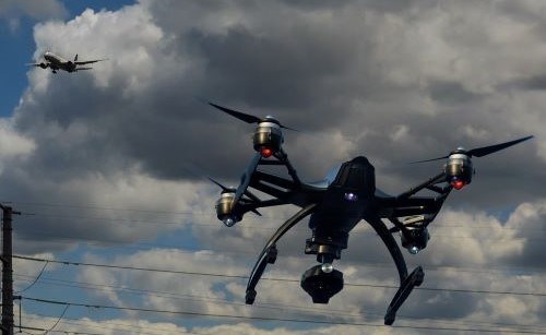 A drone flying against a cloudy sky with a passenger jet flying in the background
