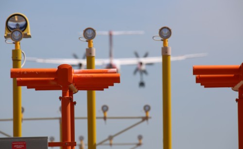 Poles with aerodrome equipment on them with a plane landing in the background