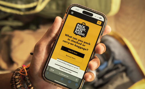 A hand holding a mobile phone displaying the Pack Right. Safe Flight. webpage