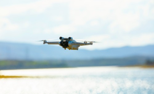 A white RPA flying with a lake in the background