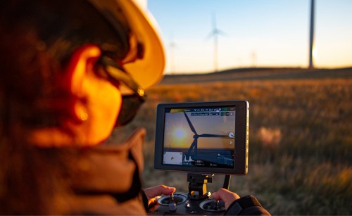 A female drone pilot flying a drone to inspect wind turbines