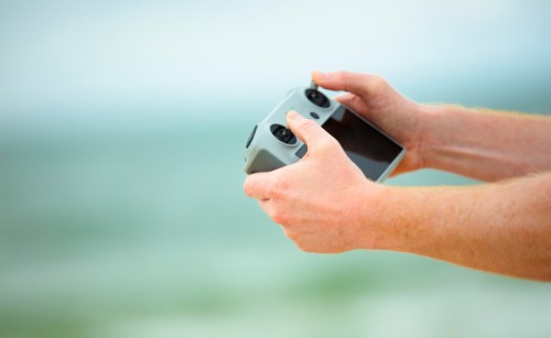 A person's hands holding a drone remote control in front of a blurry background