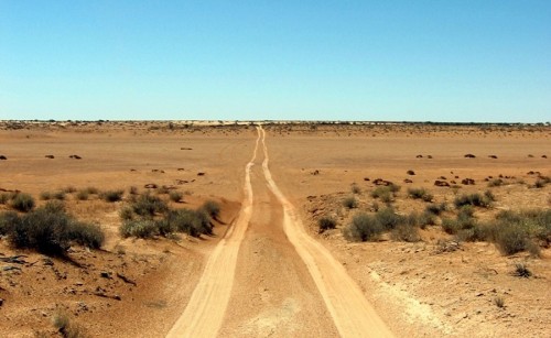 A pair of tire tracks stretching out to the desert horizon, with a clear blue sky above it