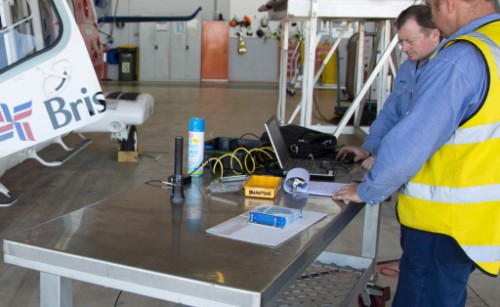 Two maintenance engineers in a hangar examining paperwork and a computer