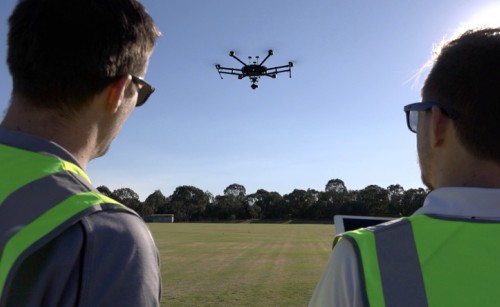 Two men in high-visibility jackets flying a drone