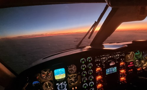 View from a cockpit in flight looking out over a sunset.