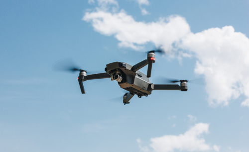 A drone flying through the blue sky, with a cloud behind it