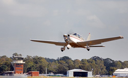 A small aeroplane taking off, with airport buildings visible behind it