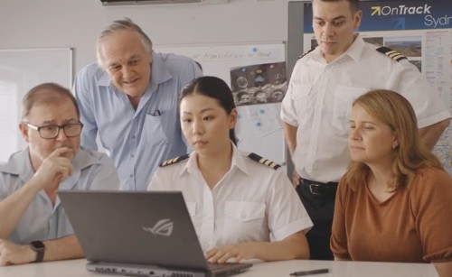 Several staff members gather around a pilot working on a laptop