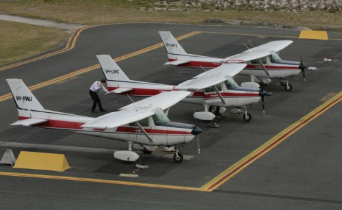 Three identical small aeroplanes lined up next to each other on the aircraft apron, as a pilot inspects the middle one
