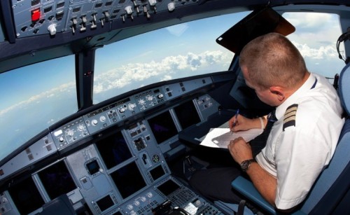 A pilot fills out documentation in the cockpit of a flying aircraft