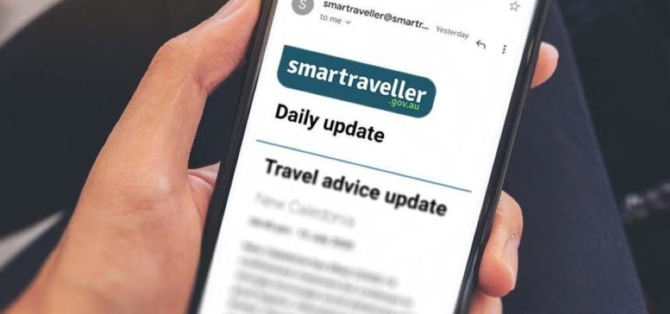 A person's hand holding a mobile phone, displaying the Smartraveller homepage on the screen