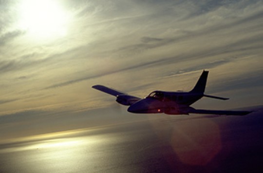 A plane flying over water, the sun reflecting beneath it