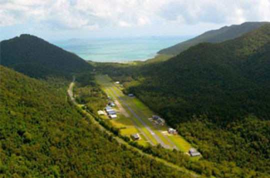 A aerial photo of a small airport surrounded by tree-covered mountains