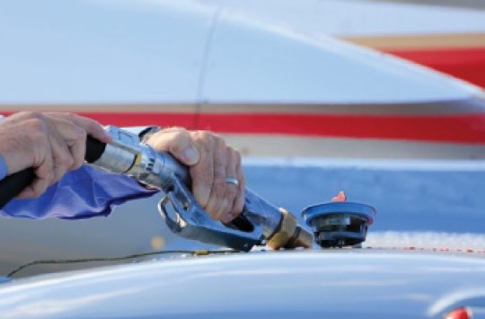 A pair of hands holding a fuel pump nozzle refuelling a plane.