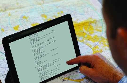 A pilot reading NOTAMs on a tablet while checking a map