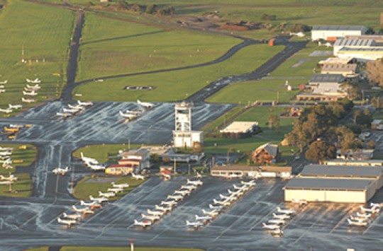 An airport with a bunch of planes parked in rows on its tarmac, with the air traffic control tower in the centre
