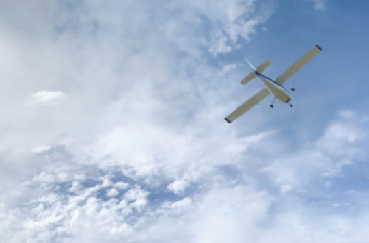 A white plane flying through a sky with wispy clouds above it