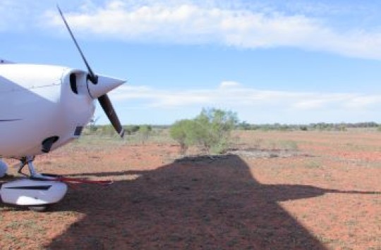 Front of a light plan propellor parked on some dirt.