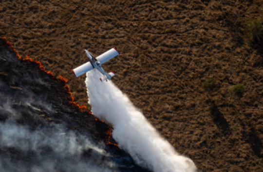 A firefighting aeroplane dropping a load of water onto the edge of a bushfire