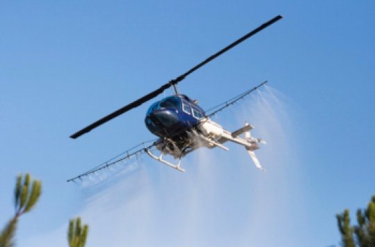 A helicopter spraying chemicals out of sprayers on its sides