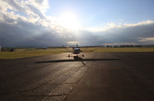 A plane sitting on a runway with the sun coming out from behind some clouds