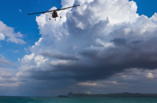 A plane flying over water with clouds in the distance