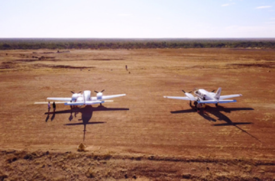 2 light planes parked in the outback on a dirt runway
