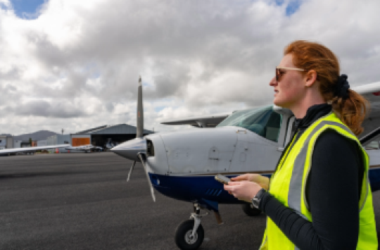 A person wearing a high-visibility vest with a small aircraft in the background