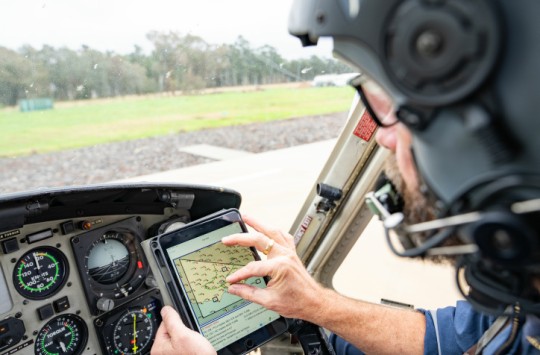 A pilot sitting in the cockpit of an aircraft on the ground, planning a flight on their electronic flight bag