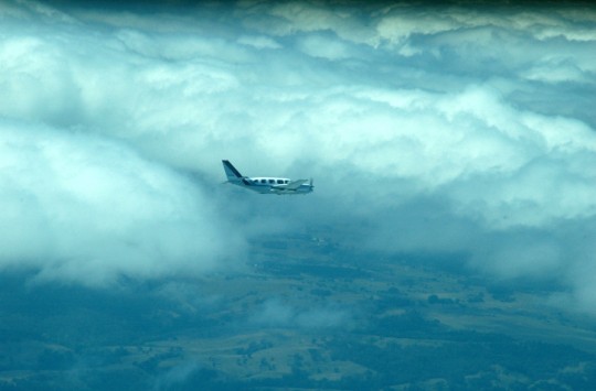 A small plane flying with clouds gathered behind it