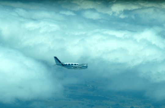An airplane flying, with thick white clouds in the background